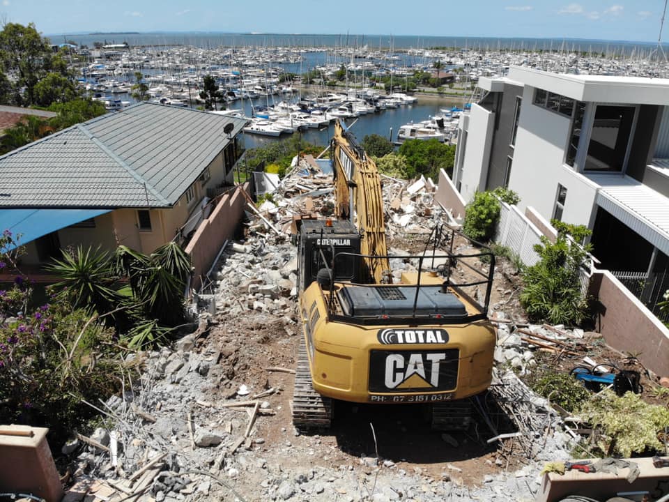 Yellow CAT heavy demolition machine demolishing a residential house near the river