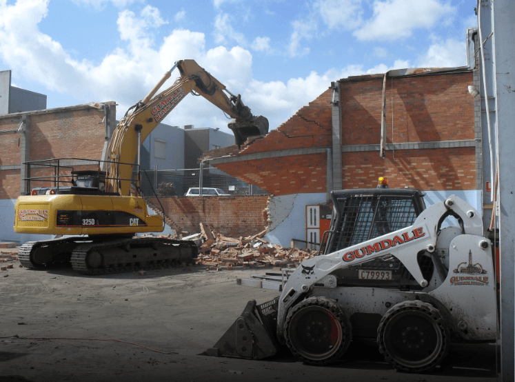 Yellow CAT heavy demolition machine demolishing a commercial brick building